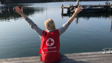 Person som sitter på brygga med ryggen till armarna i segergest. Personen har på sig en röda korset väst