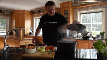 Micke Björklund kokar hjortgryta, på bilden lyfter han på grytans lock