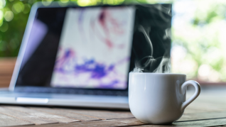kaffekopp i förgrunden, laptop i bakgrunden