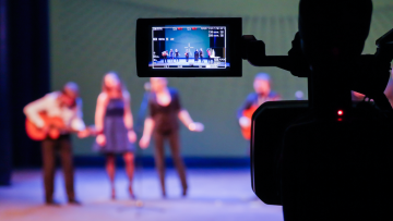 kamera i förgrunden uppträdande på scen i bakgrunden