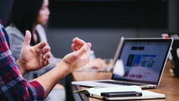 person gestikulerar framför dataskärm